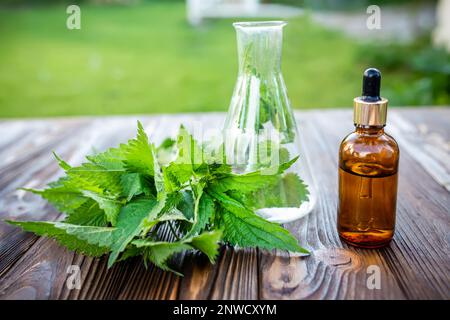 Fresh nettle and a pharmacist tube on a wooden table. Production of cosmetics and products for scalp and hair from nettle. Stock Photo