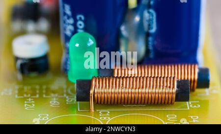 Electromagnetic coils, green LED light and electronic components on printed circuit board. Closeup of cylindric inductors or light-emitting diode. PCB. Stock Photo