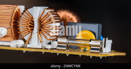 Glass electric fuse or toroid coils copper wire in hovering circuit board on black background. Inductors covered white plastic fixed by silicone paste. Stock Photo