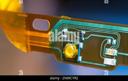 Plastic strip of flexible printed circuit and electronic surface mounted components. Closeup of green and yellow lines on PCB dismantled of headphones. Stock Photo