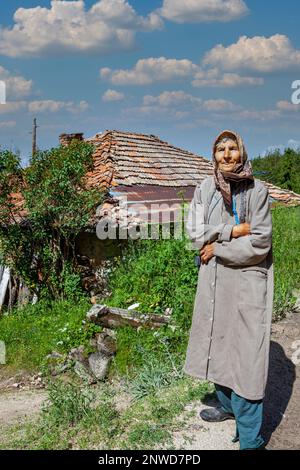 An old farmer woman standing in front of her house, Orcevo village; Belica municipality Stock Photo
