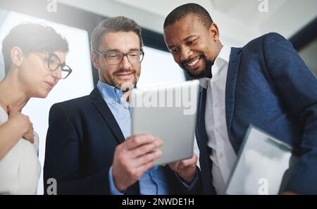 The right team with the right tools for the job. Shot of a team of colleagues using a digital tablet together at work. Stock Photo