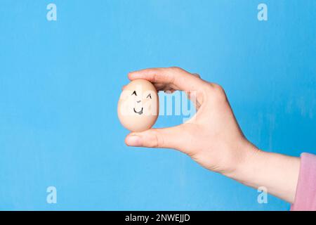 Hand holding easter egg with a funny face drawn on it. Easter or healthy diet eating concept Stock Photo