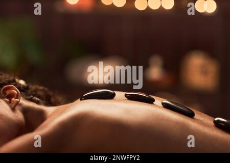 Hot basalt stone on beautiful back of young woman enjoying spa procedure Stock Photo