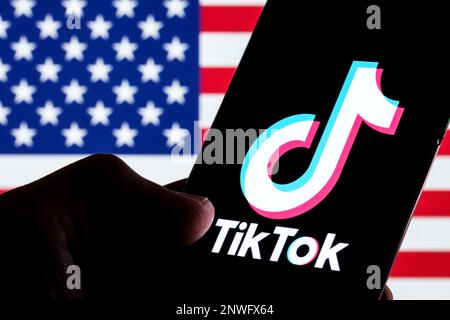 TikTok app logo seen on smartphone screen. U.S. US flag o the blurred background. Stafford, UK, February 28, 2023 Stock Photo