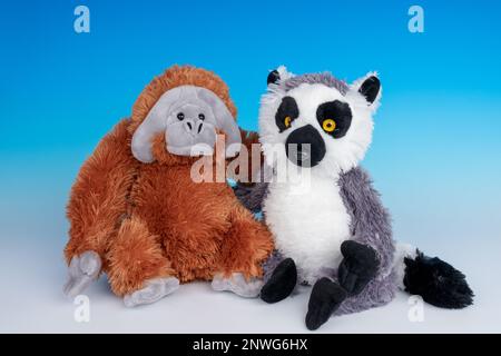 Two friendly stuffed animals (Orangutan and Ring-tailed Lemur) on a blue and white seamless background. Stock Photo
