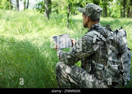Soldier with backpack using tablet in forest Stock Photo