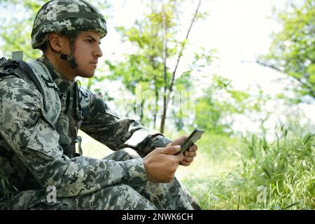 Soldier with backpack using tablet in forest Stock Photo