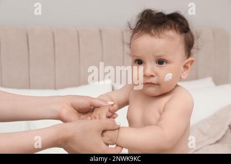 Mother applying body cream on her baby in bedroom Stock Photo
