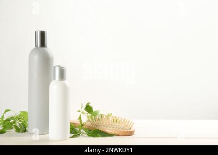 Stinging nettle, cosmetic products and brush on white wooden background, space for text. Natural hair care Stock Photo