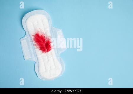 Menstrual pad with red feather on light blue background, top view. Space for text Stock Photo
