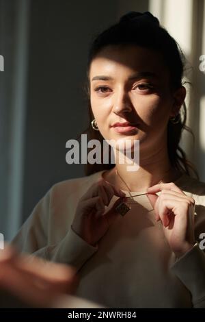 Portrait of serious young woman putting on jewelry Stock Photo