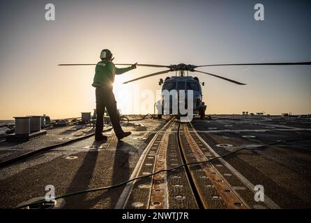 BALTIC SEA (Jan. 13, 2023) Aviation Structural Mechanic Airman Aiden Petric signals to the pilots in a MH-60R Seahawk helicopter, attached to Helicopter Maritime Strike Squadron (HSM) 79, on the flight deck aboard the Arleigh Burke-class guided-missile destroyer USS Roosevelt (DDG 80), Jan. 13, 2023. Roosevelt is on a scheduled deployment in the U.S. Naval Forces Europe area of operations, employed by U.S. Sixth Fleet to defend U.S., allied and partner interests. Stock Photo