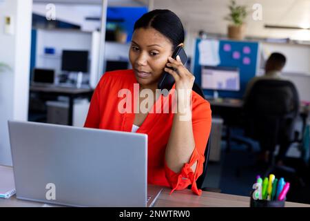 African american businesswoman using laptop and talking on smartphone at office. Working at office, business, finances and corporation concept. Stock Photo
