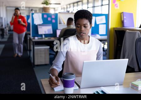 African american businesswoman using laptop and taking notes at office. Working at office, business, finances and corporation concept. Stock Photo