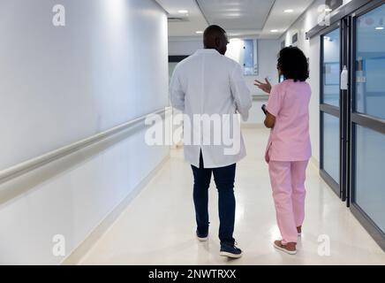 Diverse male and female doctors walking and talking in hospital. Health, hospital ward and care concept. Stock Photo