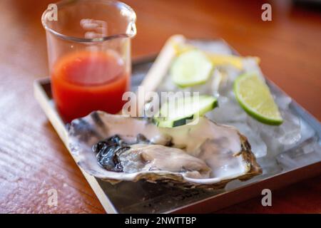 Single oyster with cocktail sauce and lemon, lime Stock Photo