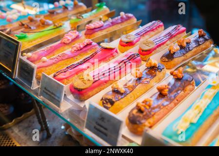 eclairs with colorful topping a lot on shop window, store shelf. french dessert, different types Stock Photo