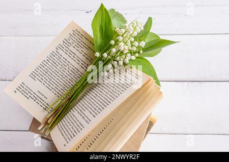 a bouquet of delicate fragrant lilies of the valley lies on an open book and a white wooden table. the concept of a good mood, a spring morning Stock Photo