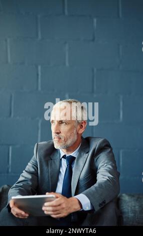 Hes got big things on his mind. a handsome and thoughtful mature businessman using a digital tablet in his office. Stock Photo