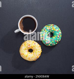 Cup of coffee and two donuts on black stone background, top view Stock Photo