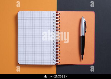 Notebook and pen on black-orange background, top view Stock Photo