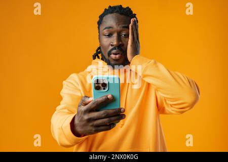 Worried black man checking phone against yellow background Stock Photo