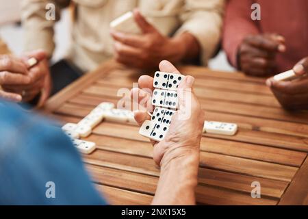 Hands, dominoes and friends in board games on wooden table for fun activity, social bonding or gathering. Hand of domino player holding rectangle Stock Photo