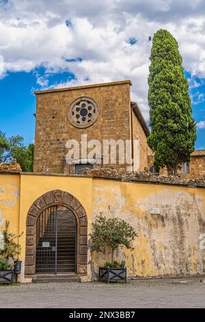 The façade with the rose window of the ex Church of Santa Croce with the entrance to the municipal gardens and the tall cypress. Tuscania, Viterbo pro Stock Photo