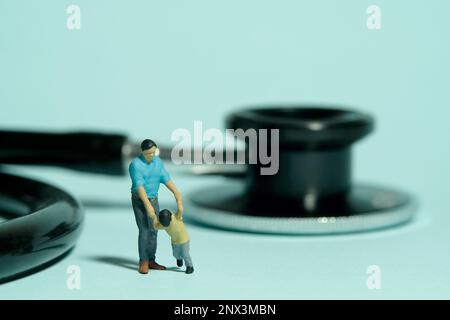 Miniature people toy figure photography. Health medical check refuses concept. A father and son standing in front of stethoscope. Isolated blue backgr Stock Photo