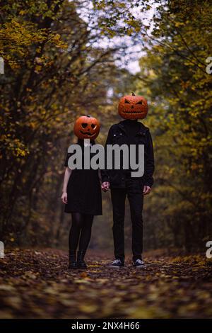 A happy couple holding pumpkin heads on their faces enjoys a fall walk down a path Stock Photo