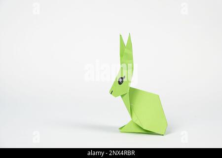 A green origami rabbit on a white background. Crafts for Easter, fold from paper, do it yourself, place for text. Stock Photo