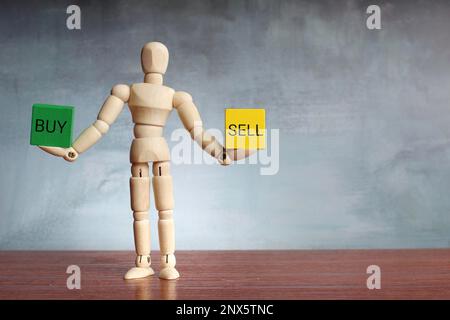 Wooden human figure balancing wooden cubes with text BUY and SELL. Business concept Stock Photo