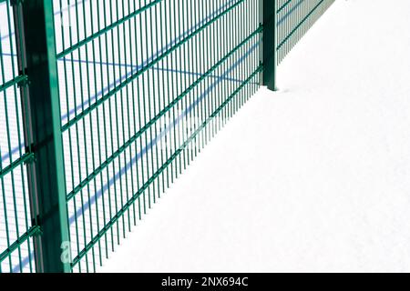 Bright green metal fence. Snowy ground. The picture was taken on a sunny winter day. Fence casts shadows in the snow. Stock Photo