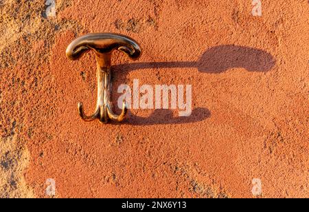 Metal hanger on old plastered wall with grazing light and projected shadow, texture with copy space Stock Photo