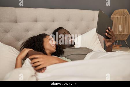 Smiling multiracial couple using a tablet in their bed Stock Photo