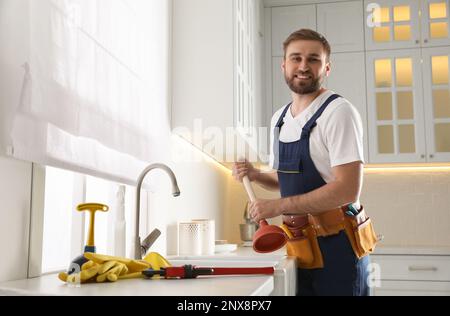 Plumber with plunger near clogged sink in kitchen Stock Photo