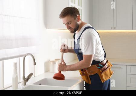 Plumber using plunger to unclog sink drain in kitchen Stock Photo