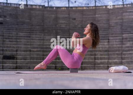 A young caucasian woman is exercising while sitting on a yoga block Stock Photo