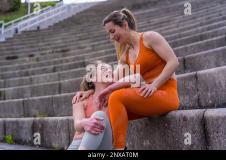 Young women sitting together on stairs smiling looking at each other Stock Photo