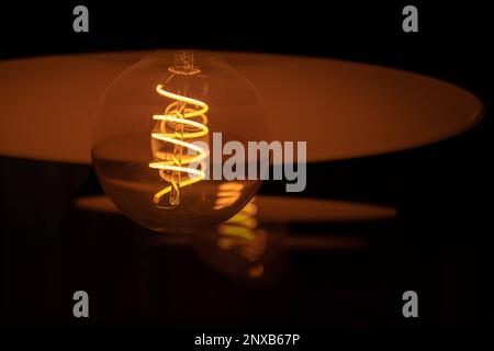 an old light bulb glowing orange in the dark Stock Photo