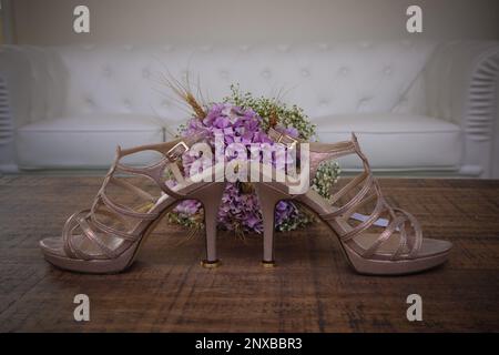 Close-up of a pair of high heel shoes and a wedding bouquet on a table in front of a sofa Stock Photo