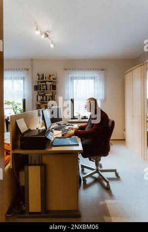 Side view of senior man using computer at desk in home office Stock Photo