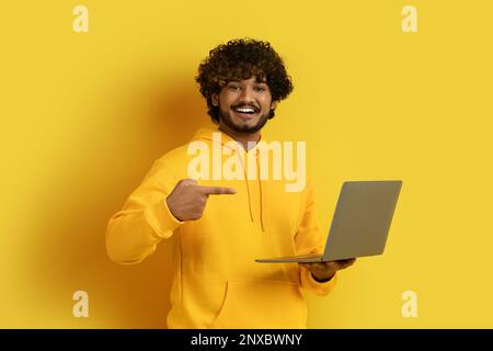 Positive curly indian man using laptop on yellow Stock Photo