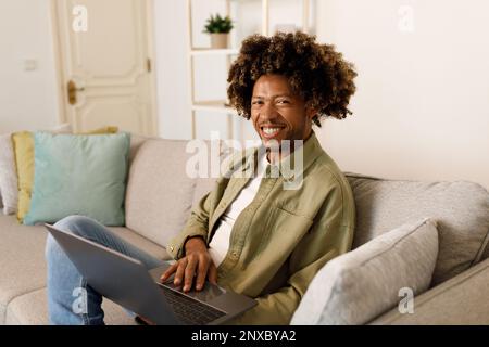 Happy Black Man Using Laptop Sitting On Sofa At Home Stock Photo