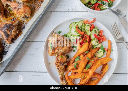 Chicken drumsticks and shanks with sweet potato fries and mediterranean zucchini, pepper salad on a plate Stock Photo