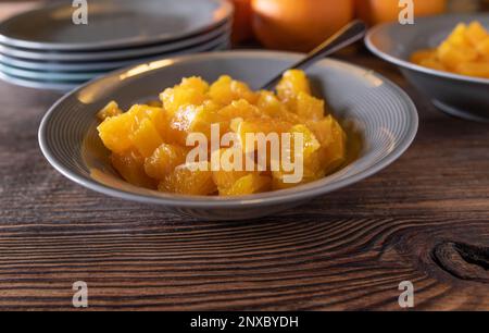 Chopped oranges in a bowl with spoon for dessert or snack on wooden table. Closeup, front view with copy space Stock Photo