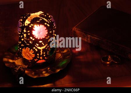 Night light. Antique glass and metal tea light candle/tea light holder, bible and rings on a bedside table Stock Photo