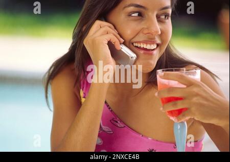 Woman using mobile phone, holding tropical drink near pool, close-up Stock Photo
