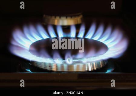 Abstract of a blue gas or propane flame of a kitchen cook stove in darkness. Selective focus on aluminum burner with blurred foreground an background Stock Photo